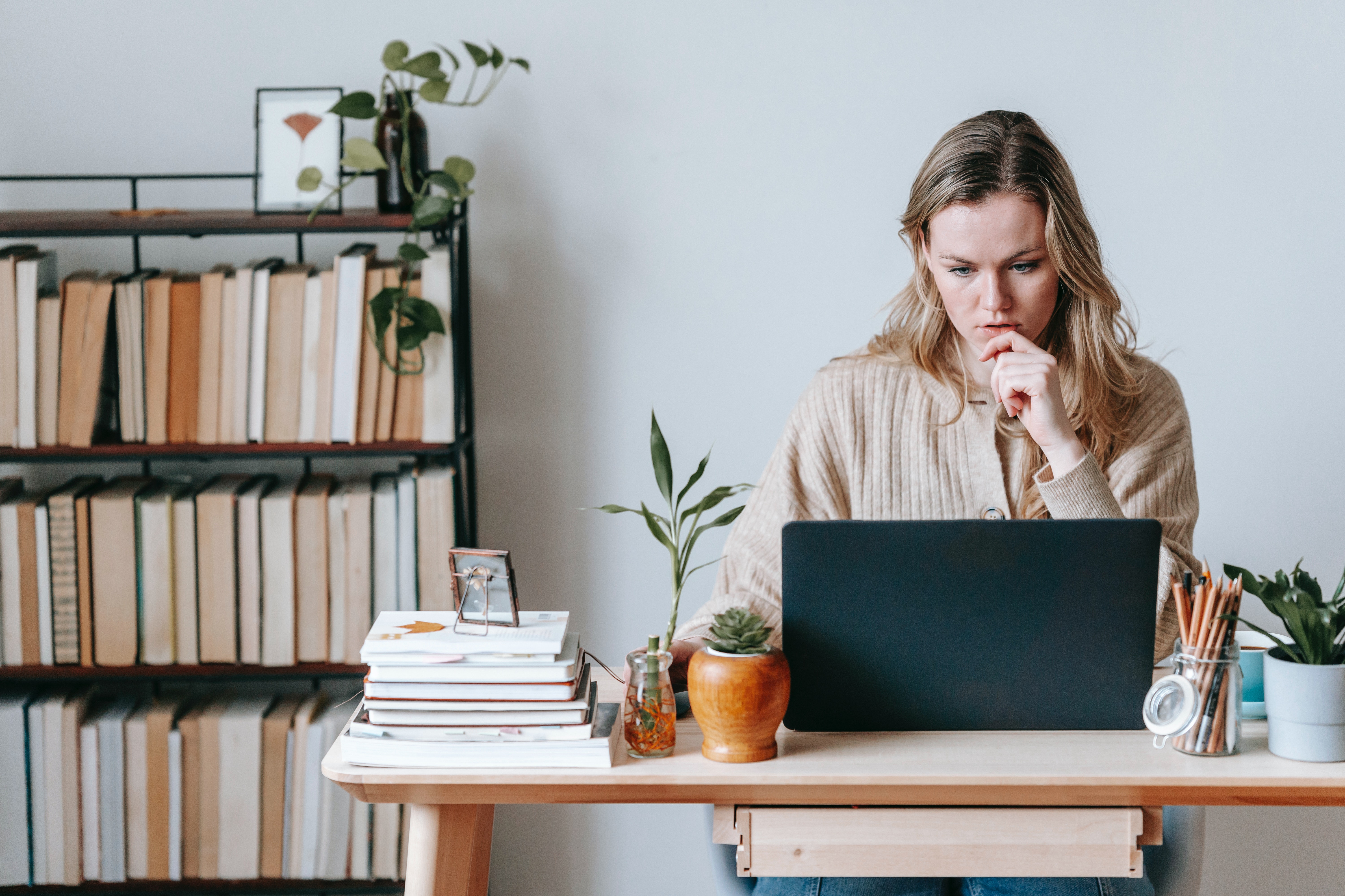 Pensive woman browsing laptop near books